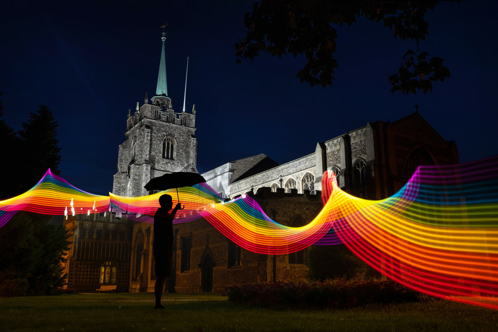 A Man In Silhouette Stands In Front Of Chelmsford Cathedral At Night With A Rainbow Graphic In The Foreground