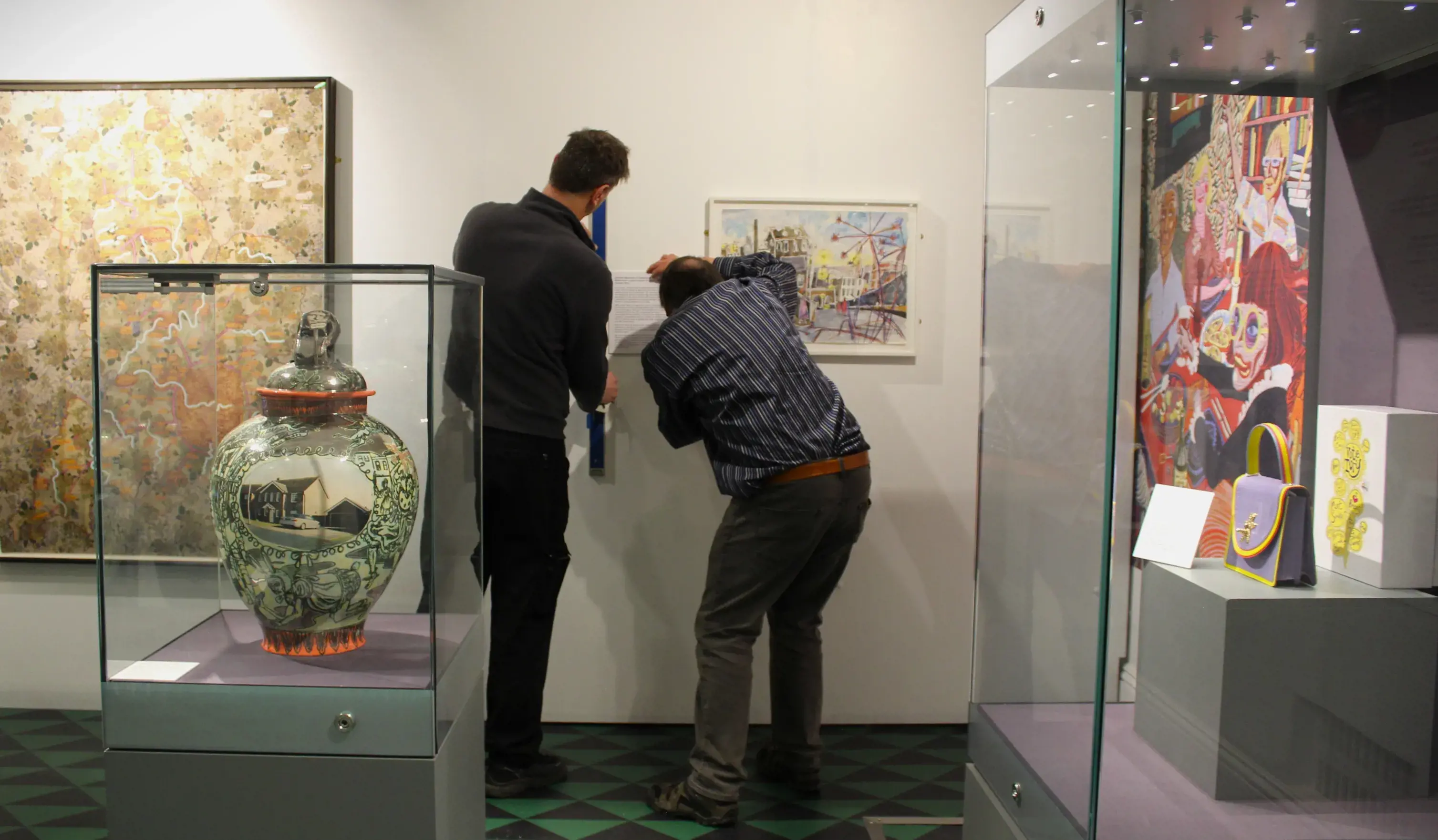 Two members of museum staff install an information panel for 'Untitled' by Grayson Perry
