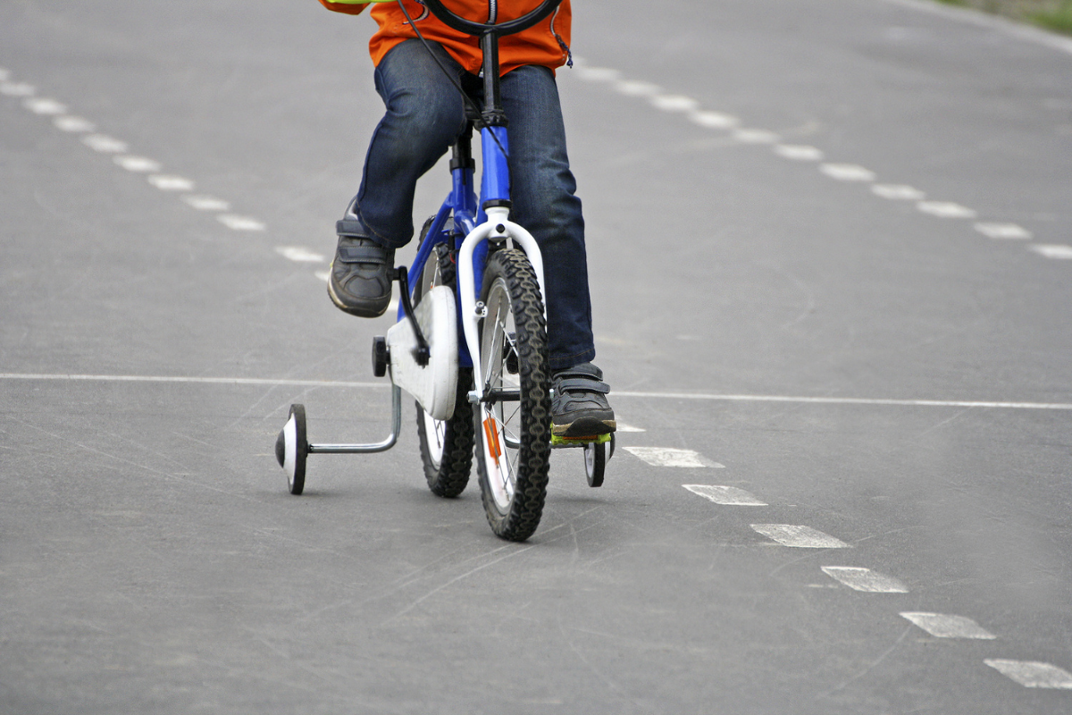 A Child Rides A Bik With Stabilisers