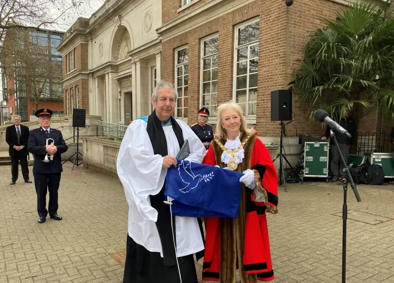 Reverend and mayor holding dove of peace flag