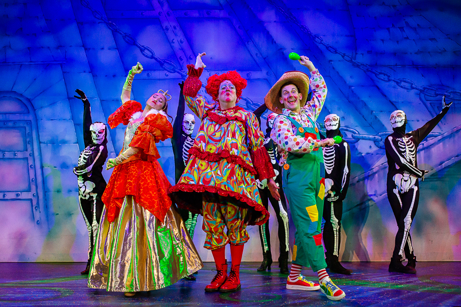2023 panto Queen Fussybutt, Dame Trott and Silly Bill on stage with skeletons.
