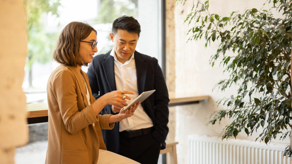 Two people standing in office environment conferring over a tablet device
