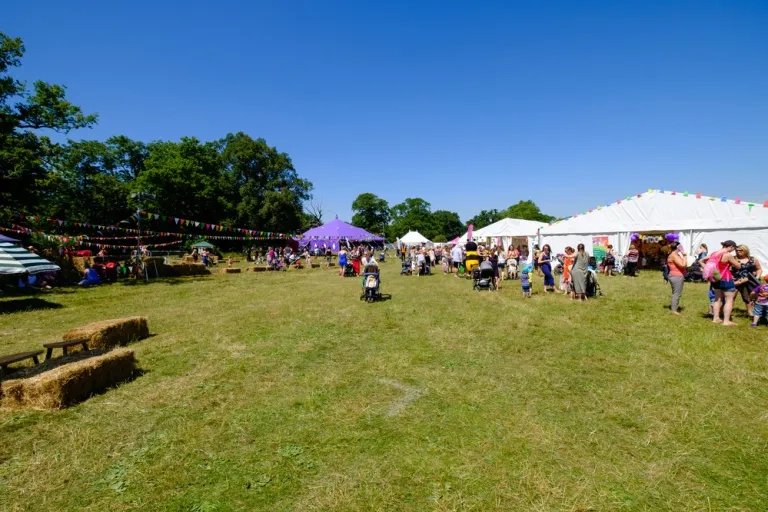 Large field on sunny day filled with tents, hay bales and families wandering around