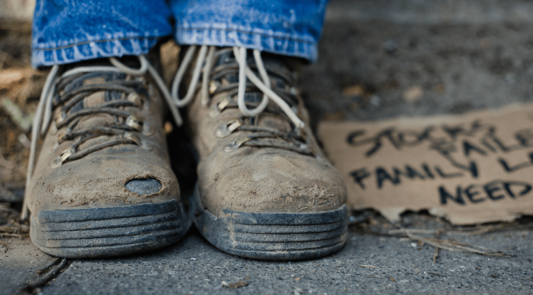 Pair of brown scuffed boots with a hand written cardboard sign beside them
