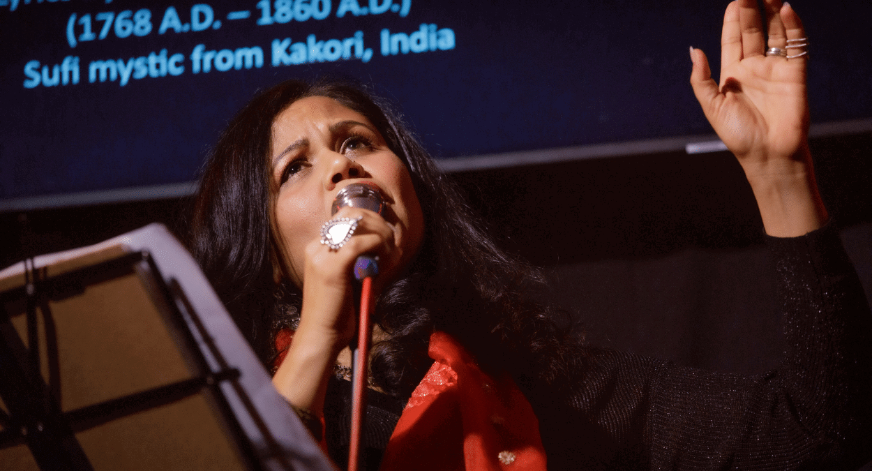 A Photo Of Poet And Musician Shephali Frost Speaking Into A Microphone On Stage