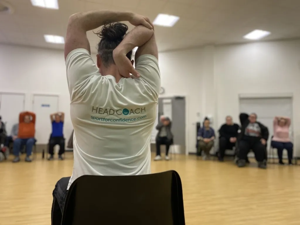 Sport For Confidence Head Coach Leads A Class In Seated Stretching