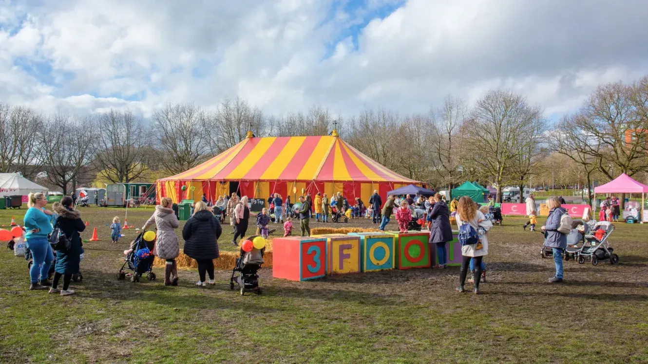 Large field with families milling around, with red and yellow stripy tent and 3Foot spelled out with big blocks
