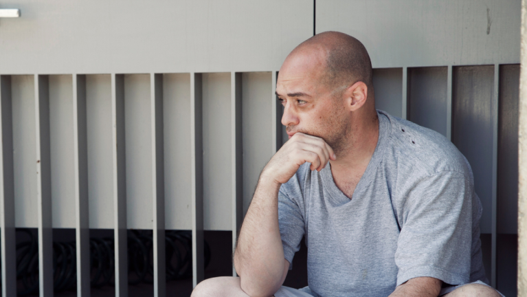 A Man Is Crouching Down On The Street Looking Contemplative