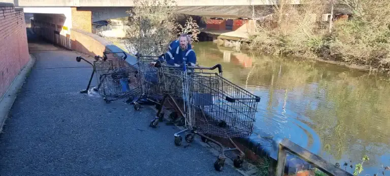 Man sitting with 4 rusted shopping trolleys pulled from river