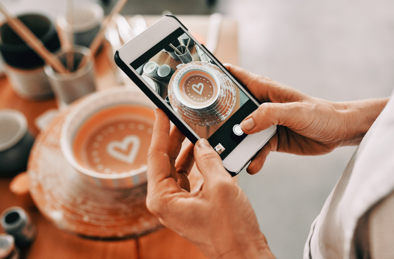 Person taking photo of coffee in mug with a heart decoration