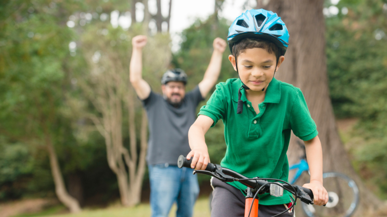 Child Learning To Ride A Bike With His Dad
