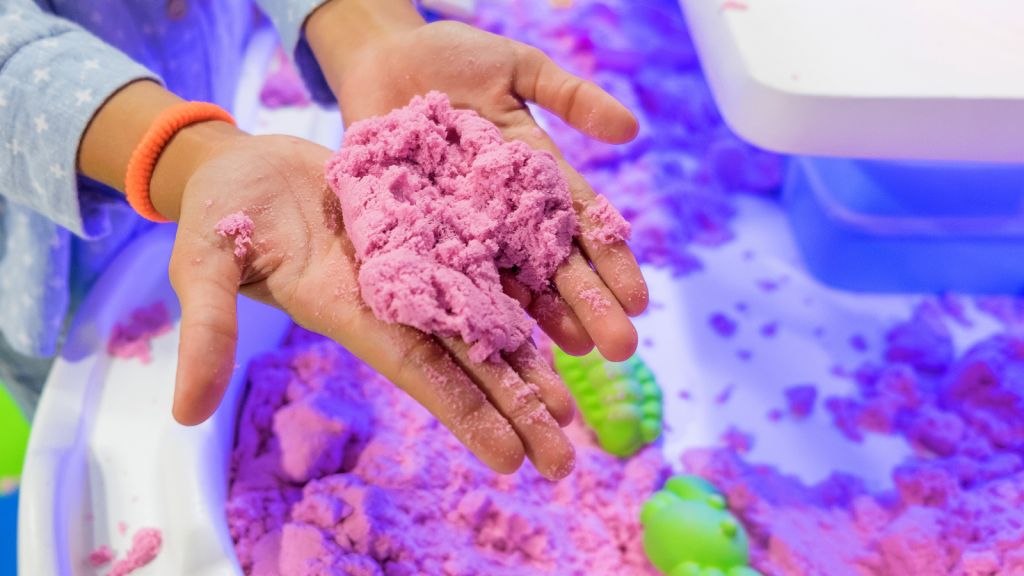 Close Up A Child's Hands Holding Up Brightly Coloured Kinetic Sand
