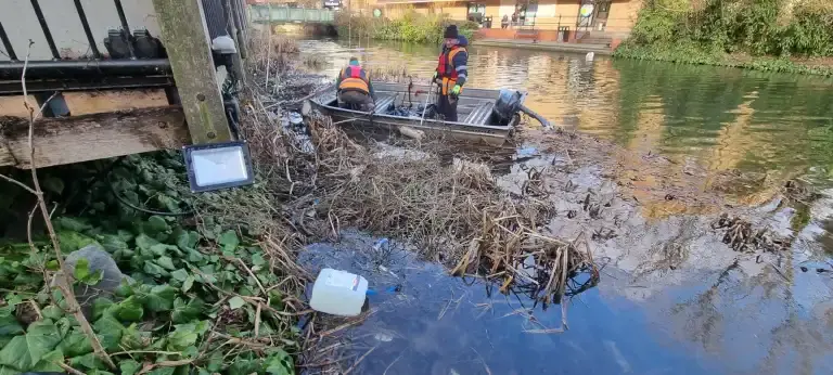 2 people on a boat searching for litter in the river
